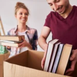 Couple packing books into a cardboard box using the Best Way to Pack Books for Moving.