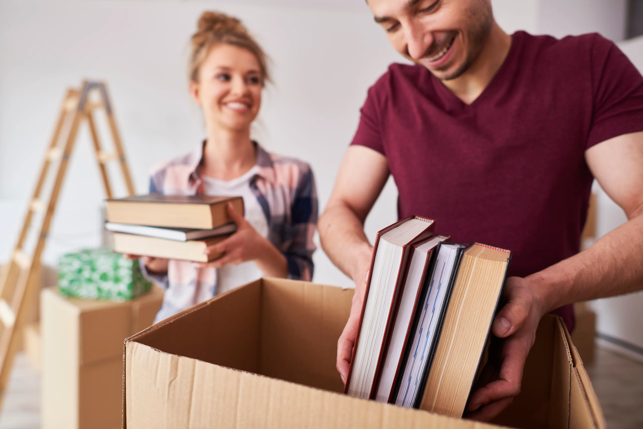 Couple packing books into a cardboard box using the Best Way to Pack Books for Moving.